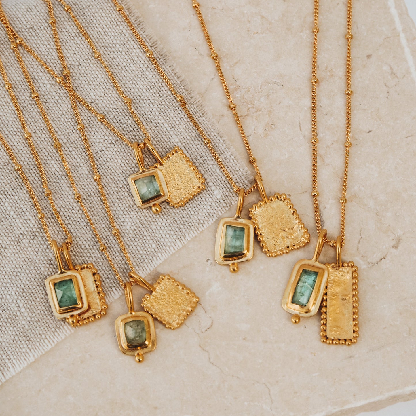 Group of artisan-crafted gold necklaces, featuring square pendants with mesmerizing ocean blue rose cut tourmaline gemstones, textured surfaces, and meticulous granulation accents