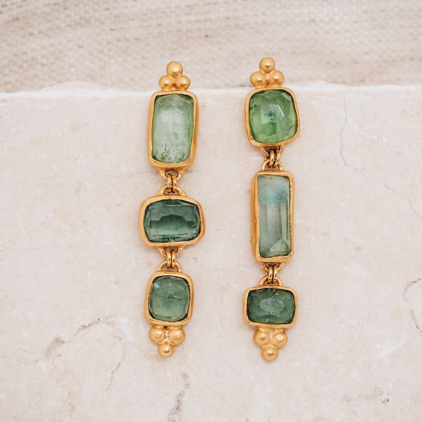earrings showcasing rich gold color with hints of blue and green, reminiscent of the serene hues of the ocean. The earrings feature organic gemstones in varying shades of blue and green, with square and rectangular rose-cut tourmalines adding a unique touch.
