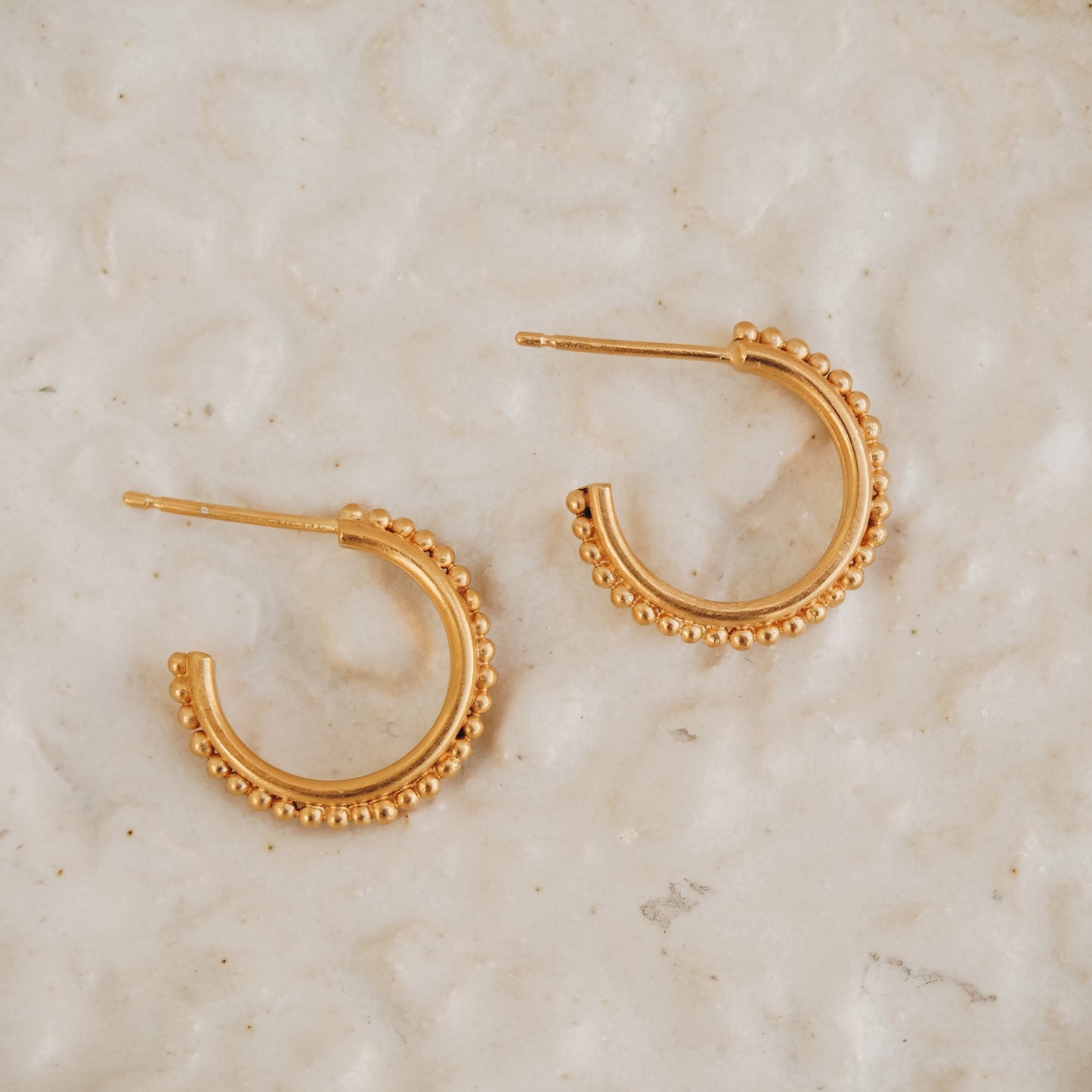 Handcrafted gold stud hoop earrings reminiscent of ancient adornment, adorned with intricate granulation.