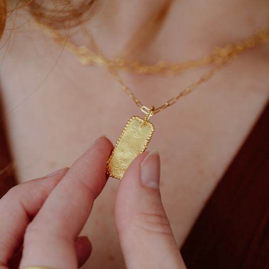 A stunning necklace featuring a rectangular pendant adorned with intricate granulation accents, set against a modern chain style in rich gold vermeil.
