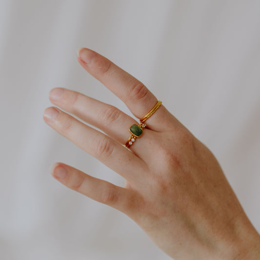 Image of a hand showcasing the artistry of artisan gold rings, adorned with delicate granulation and adorned with a beautiful forest green tourmaline gemstone.