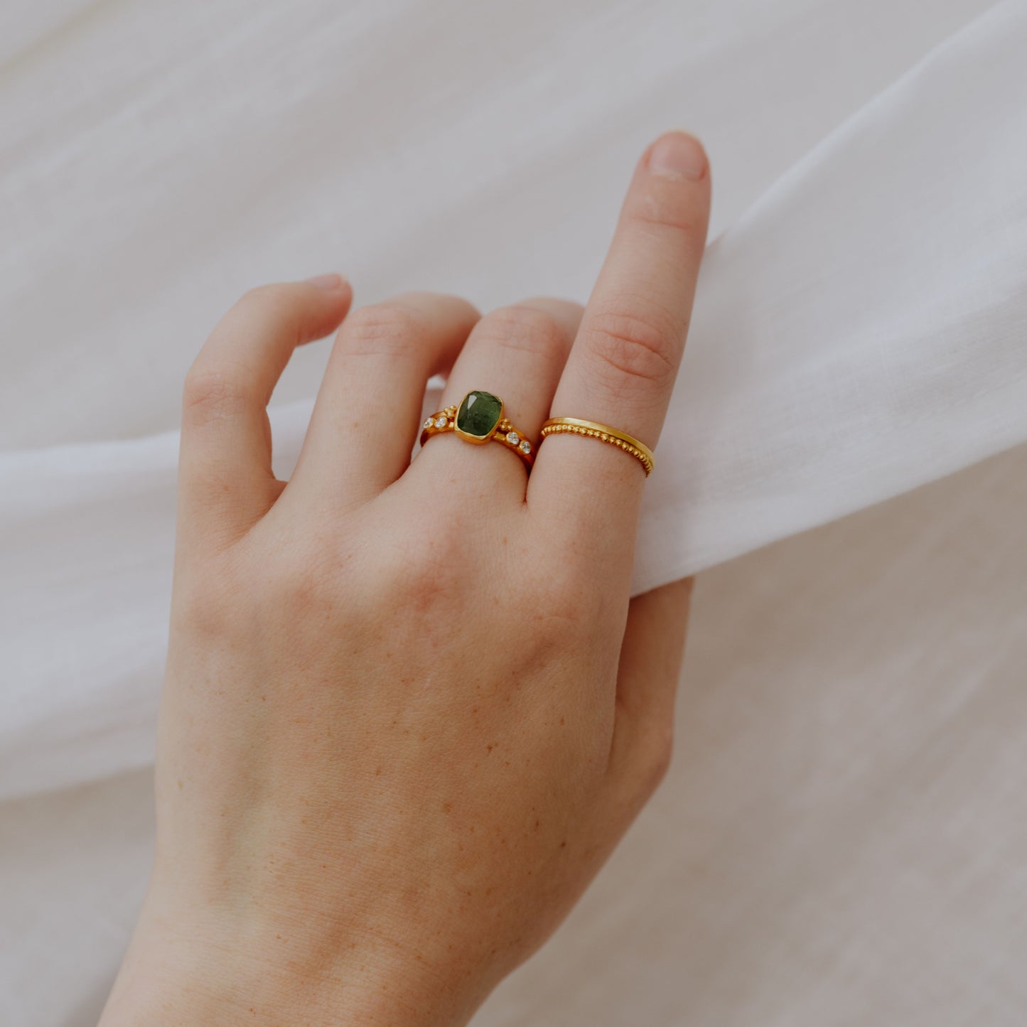 Unique handcrafted gold rings worn on an elegant hand, each with intricate granulation and adorned with a beautiful forest green tourmaline gemstone.