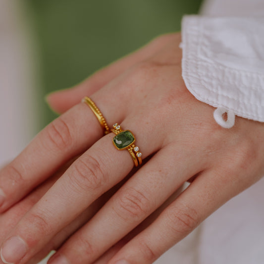Elegantly adorned fingers with handcrafted gold rings, featuring exquisite granulation detailing and stunning forest green tourmaline gemstone