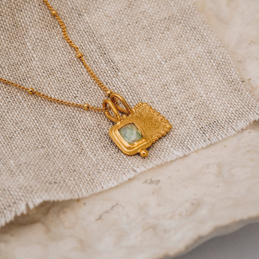A gold necklace with a pair of square granulated pendants and a blue gemstone