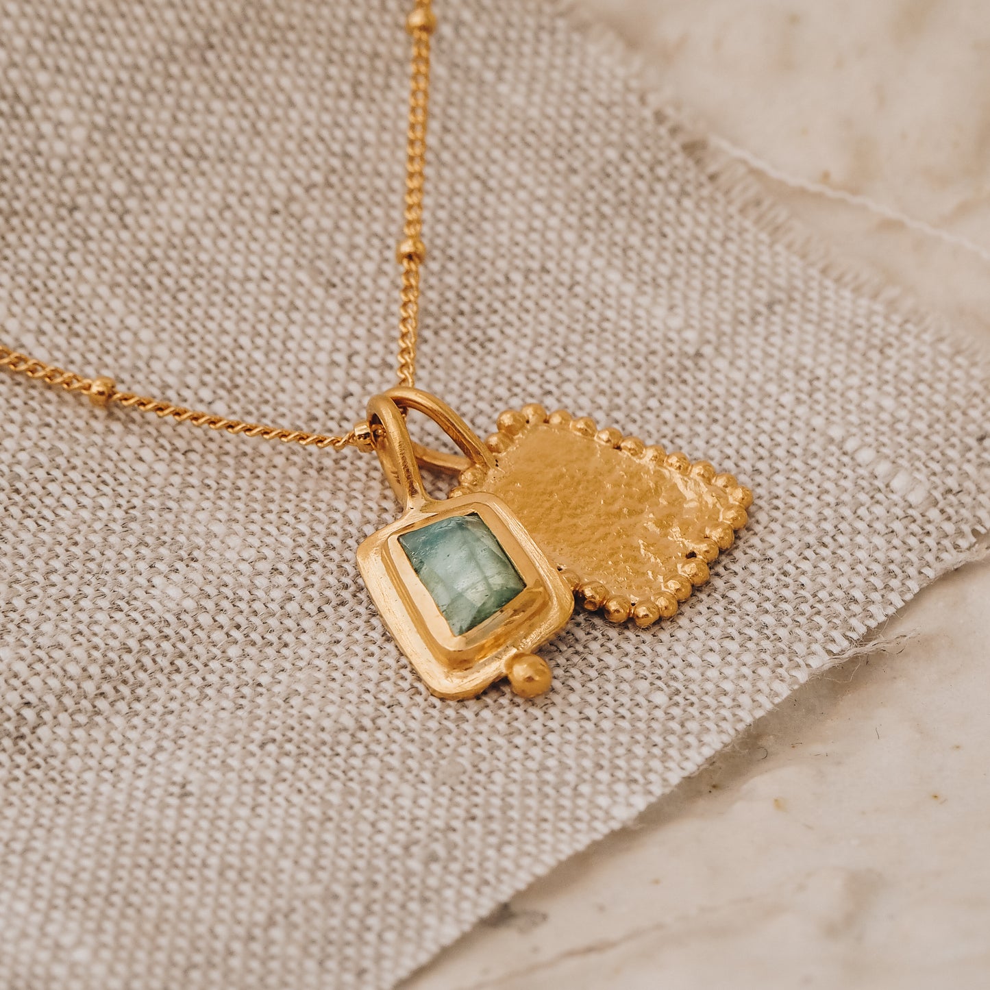 Handcrafted square gold pendant showcasing a captivating blue rose cut tourmaline gemstone and intricate granulation, hanging from a delicate satellite chain.