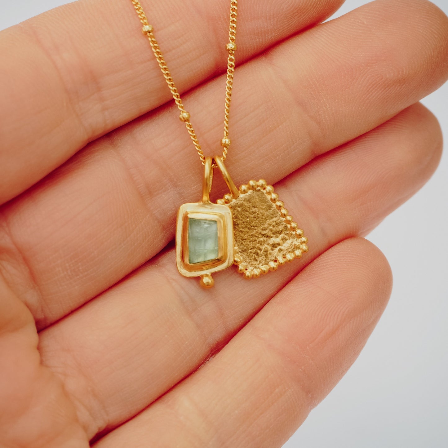 Delicate square gold pendant adorned with a mesmerizing blue rose cut tourmaline gemstone and exquisite granulation, hanging gracefully from a satellite chain.
