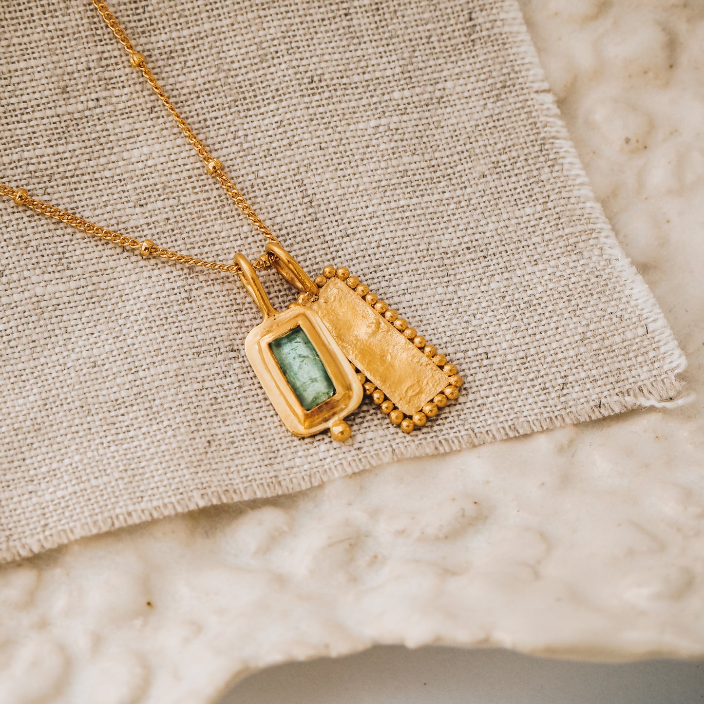 Square gold pendant showcasing a stunning blue rose cut tourmaline gemstone and meticulous granulation work, gracefully suspended from a delicate satellite chain.