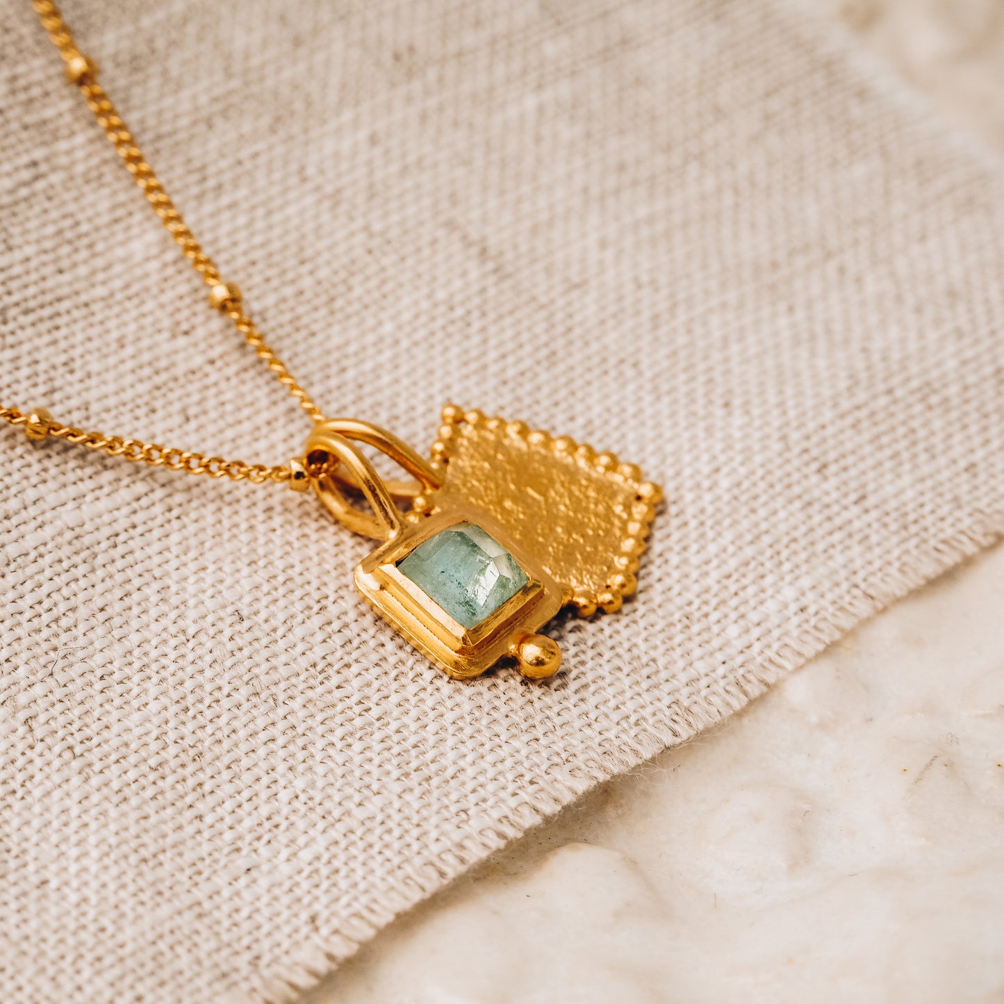 Elegant square gold pendant with a stunning blue rose cut tourmaline gemstone and delicate granulation detail, hanging from a fine satellite chain.