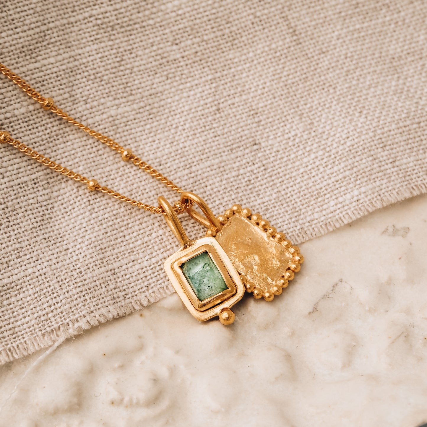 Square gold pendant showcasing a stunning blue rose cut tourmaline gemstone and meticulous granulation, suspended from a dainty satellite chain.