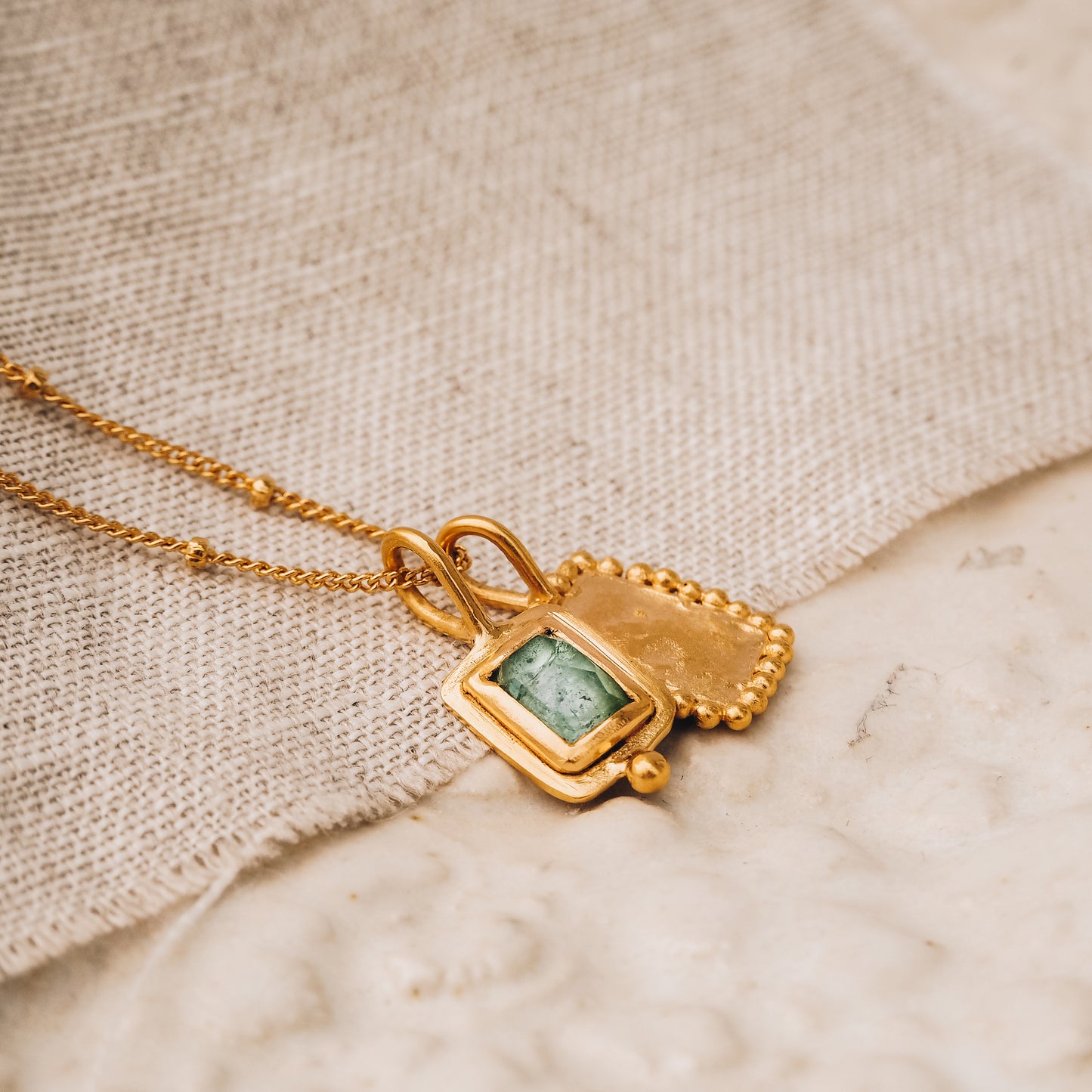 Handcrafted square gold pendant featuring a vibrant blue rose cut tourmaline gemstone and meticulous granulation detail, suspended gracefully from a delicate satellite chain.