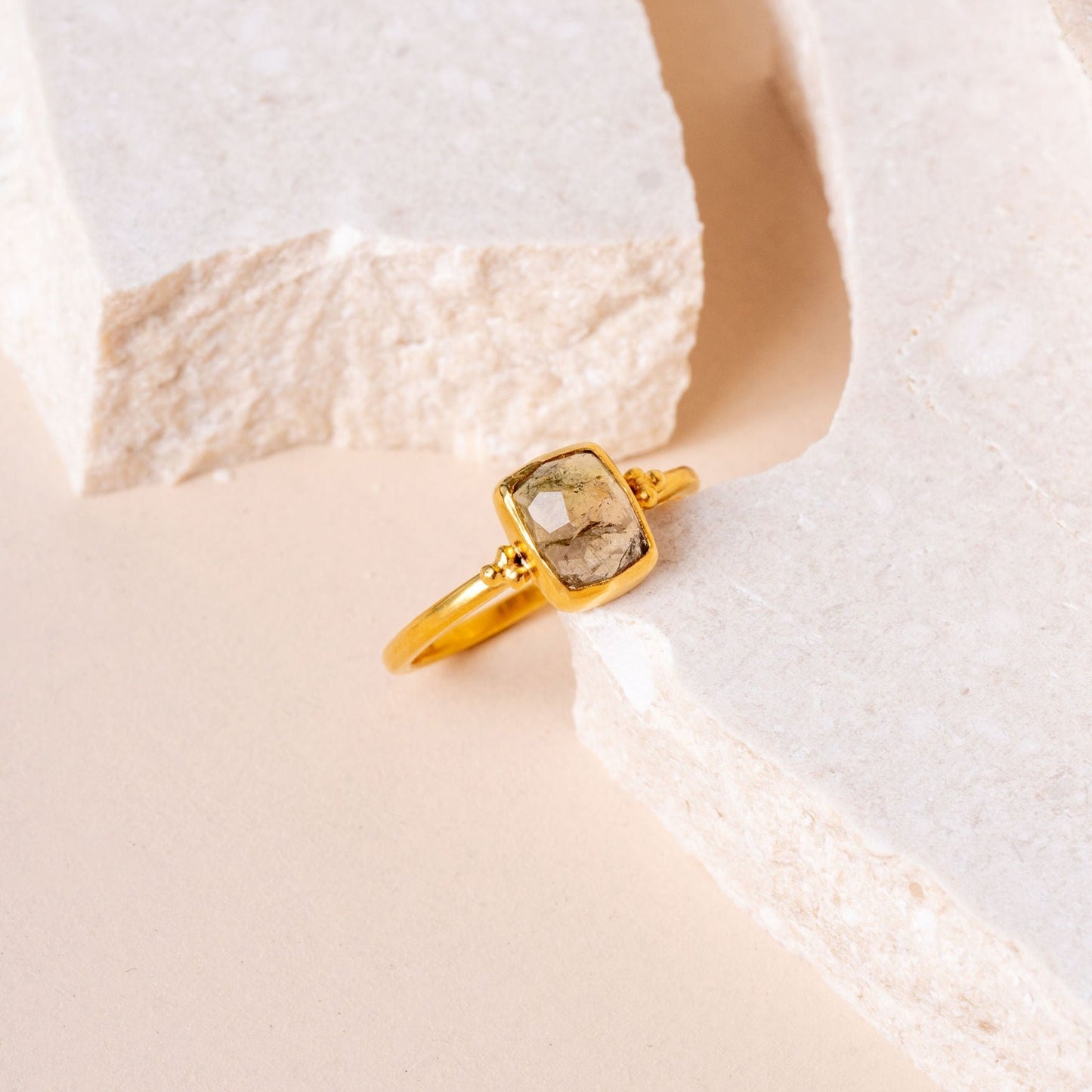 Close-up view of a handcrafted gold ring, showcasing fine granulation details and a beautiful, organic olive-colored gemstone.