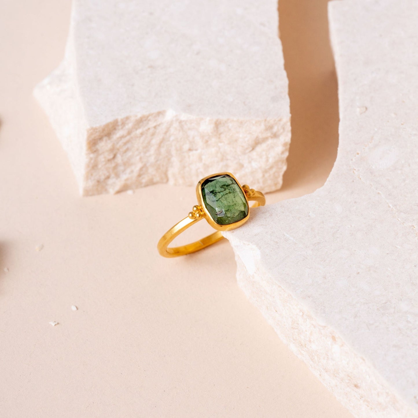 A stand-alone image showcasing the beauty of a handcrafted gold ring adorned with delicate granulation and a striking green tourmaline gemstone.
