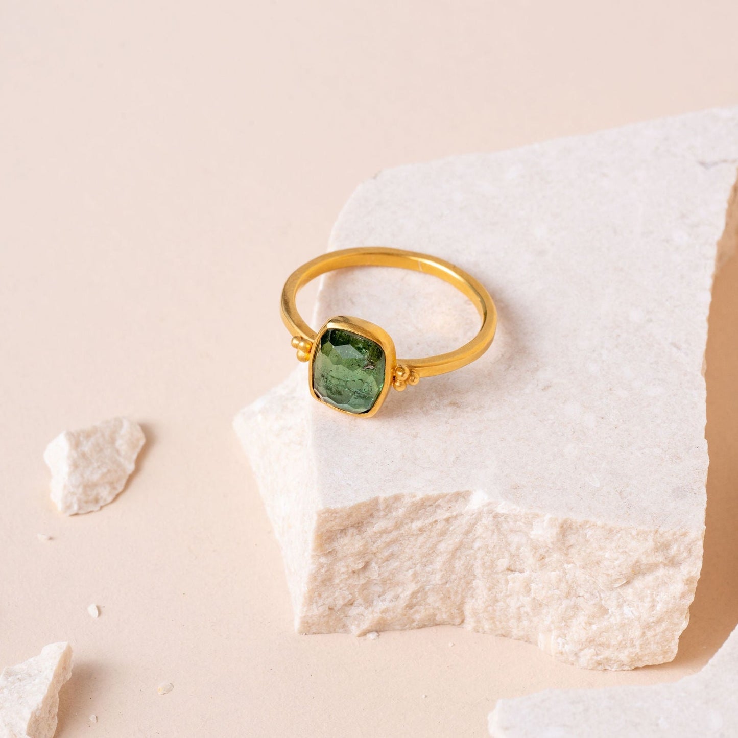 A detailed photograph of a singular gold ring, highlighting the craftsmanship of granulation and the rich hue of a green tourmaline gemstone