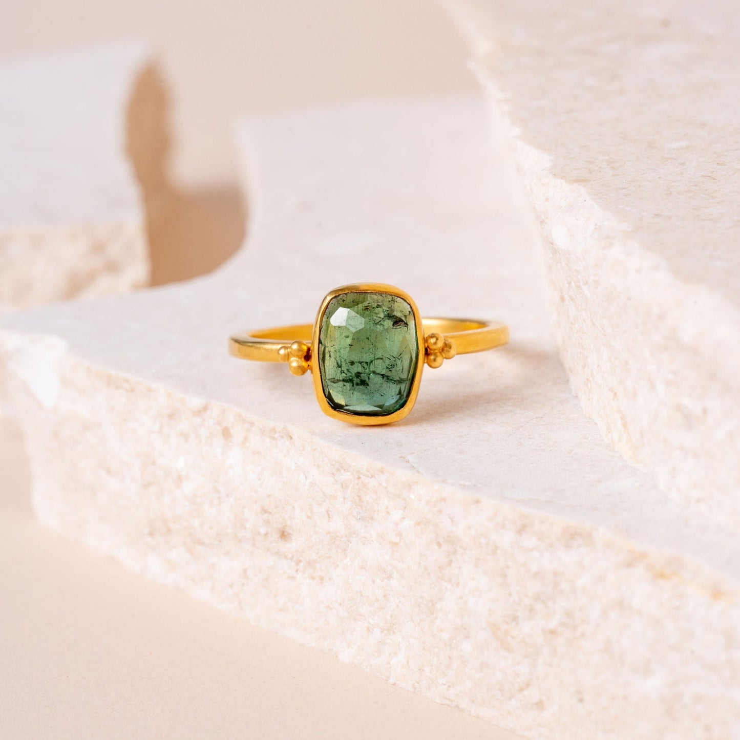 Close-up view of an exquisite gold ring, handcrafted with precision granulation and crowned by a captivating green tourmaline gemstone.