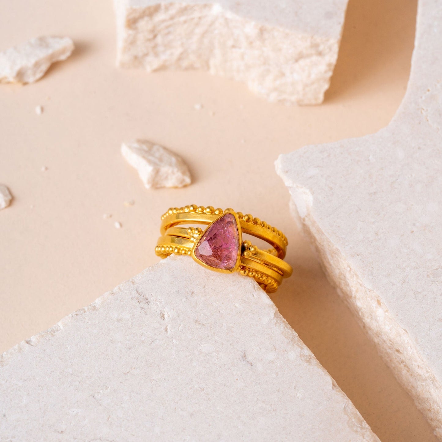A cluster of handcrafted gold rings with intricate granulation details, one adorned with a charming pink tourmaline gem.
