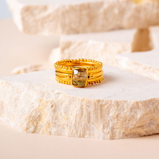 A luxurious gold ring, expertly handcrafted with delicate granulation details, encircling an exquisite olive-coloured hand-cut gemstone