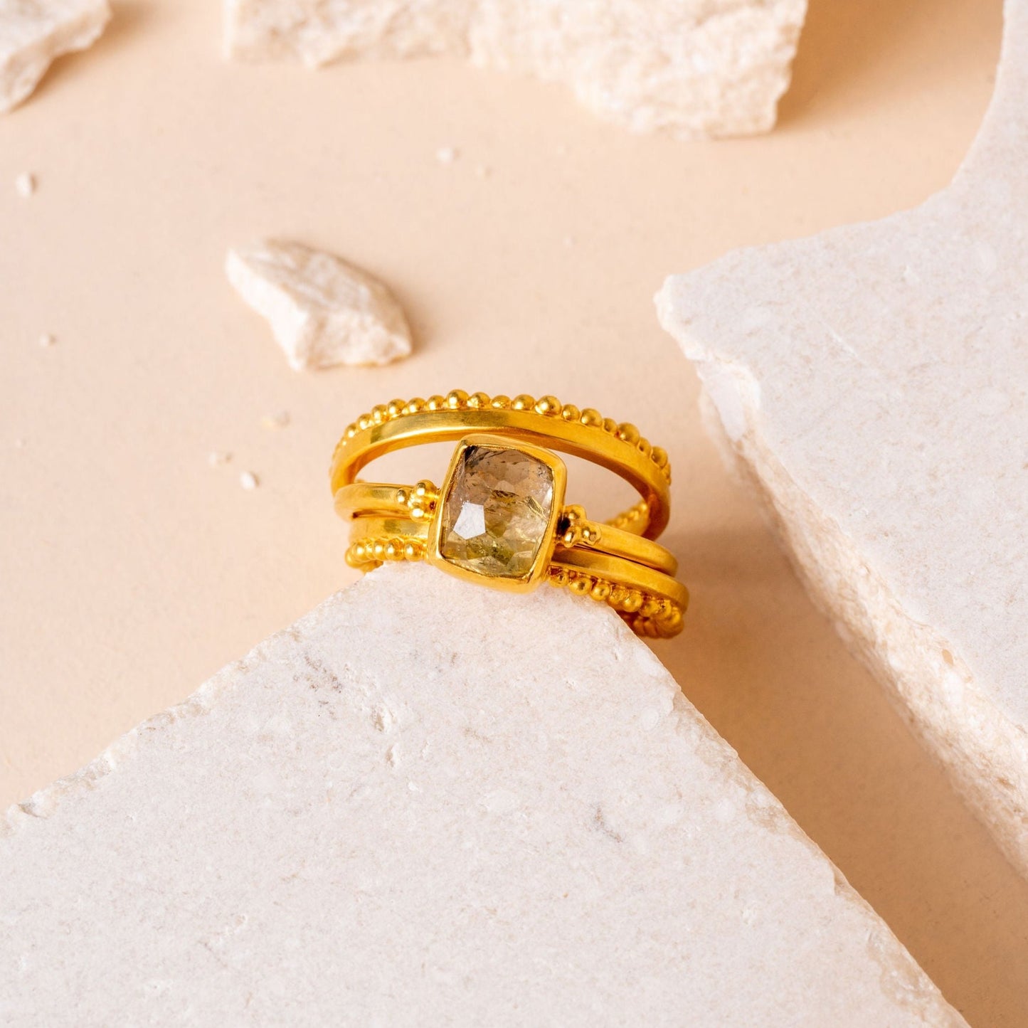Close-up view of a luxurious gold rings adorned with delicate granulation details, surrounding a mesmerizing hand-cut olive-colored gemstone.