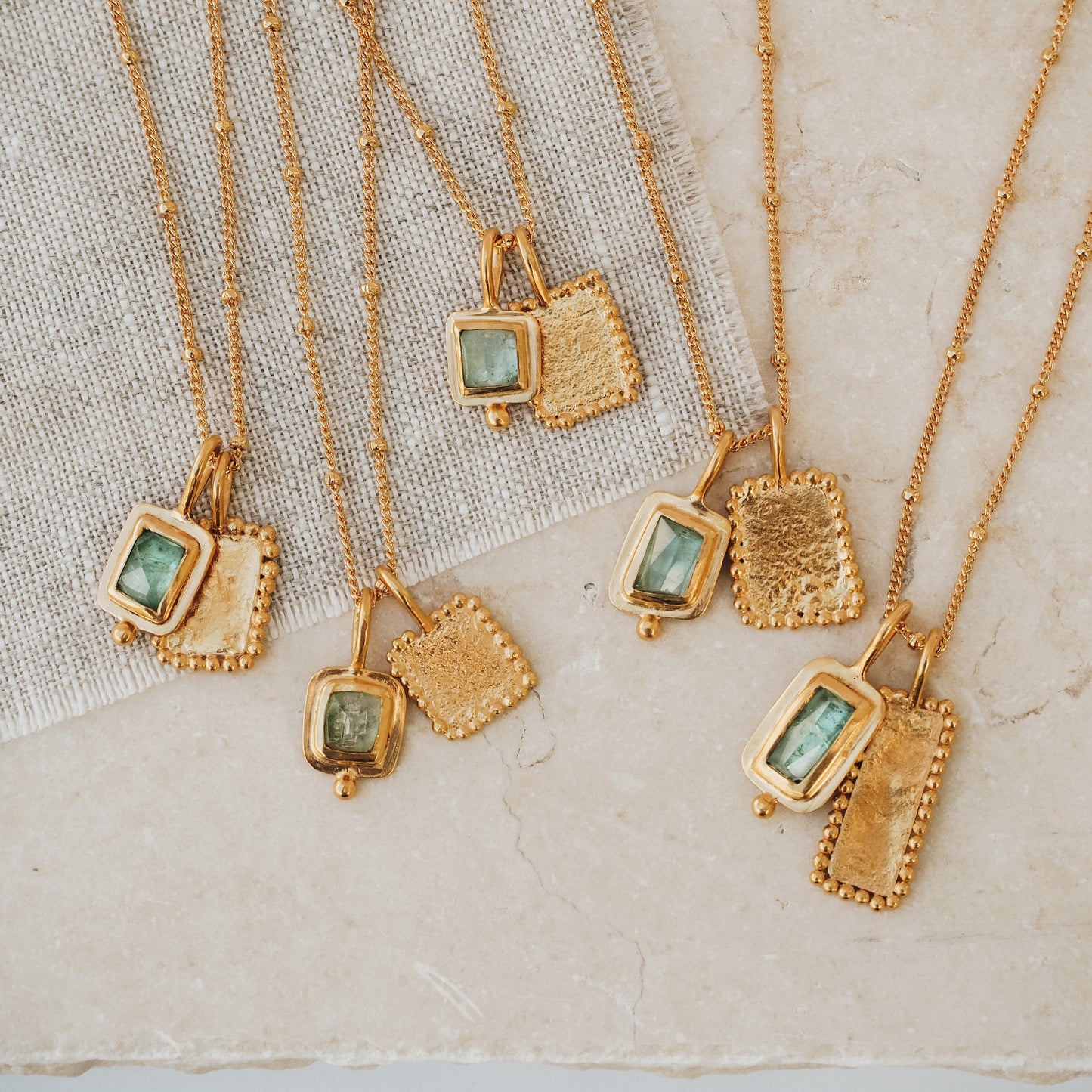 Group of elegant rich gold necklaces, featuring square pendants adorned with captivating ocean blue rose cut tourmaline gemstones, textured surfaces, and intricate granulation workmanship.
