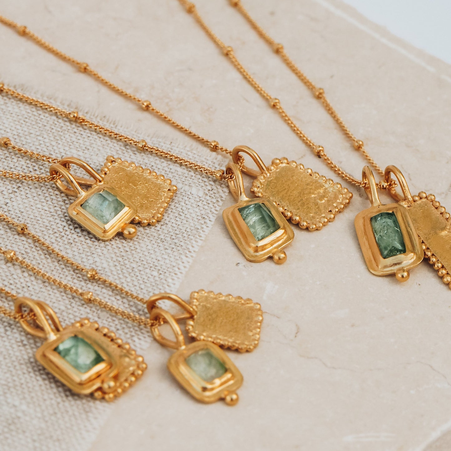 Handcrafted gold necklaces showcasing square pendants embellished with enchanting ocean blue rose cut tourmaline gemstones, textured surfaces, and intricate granulation details, creating a truly unique and captivating look.