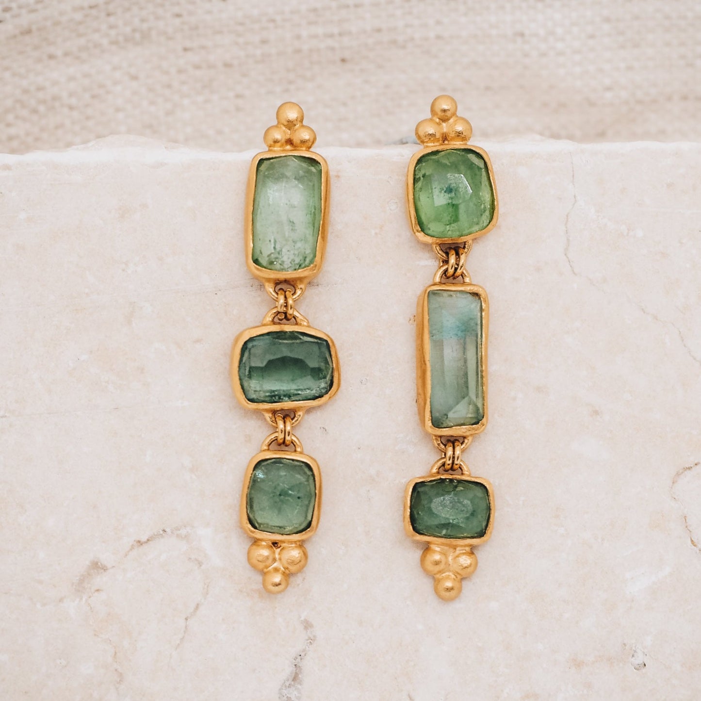 earrings showcasing rich gold color with hints of blue and green, reminiscent of the serene hues of the ocean. The earrings feature organic gemstones in varying shades of blue and green, with square and rectangular rose-cut tourmalines adding a unique touch.