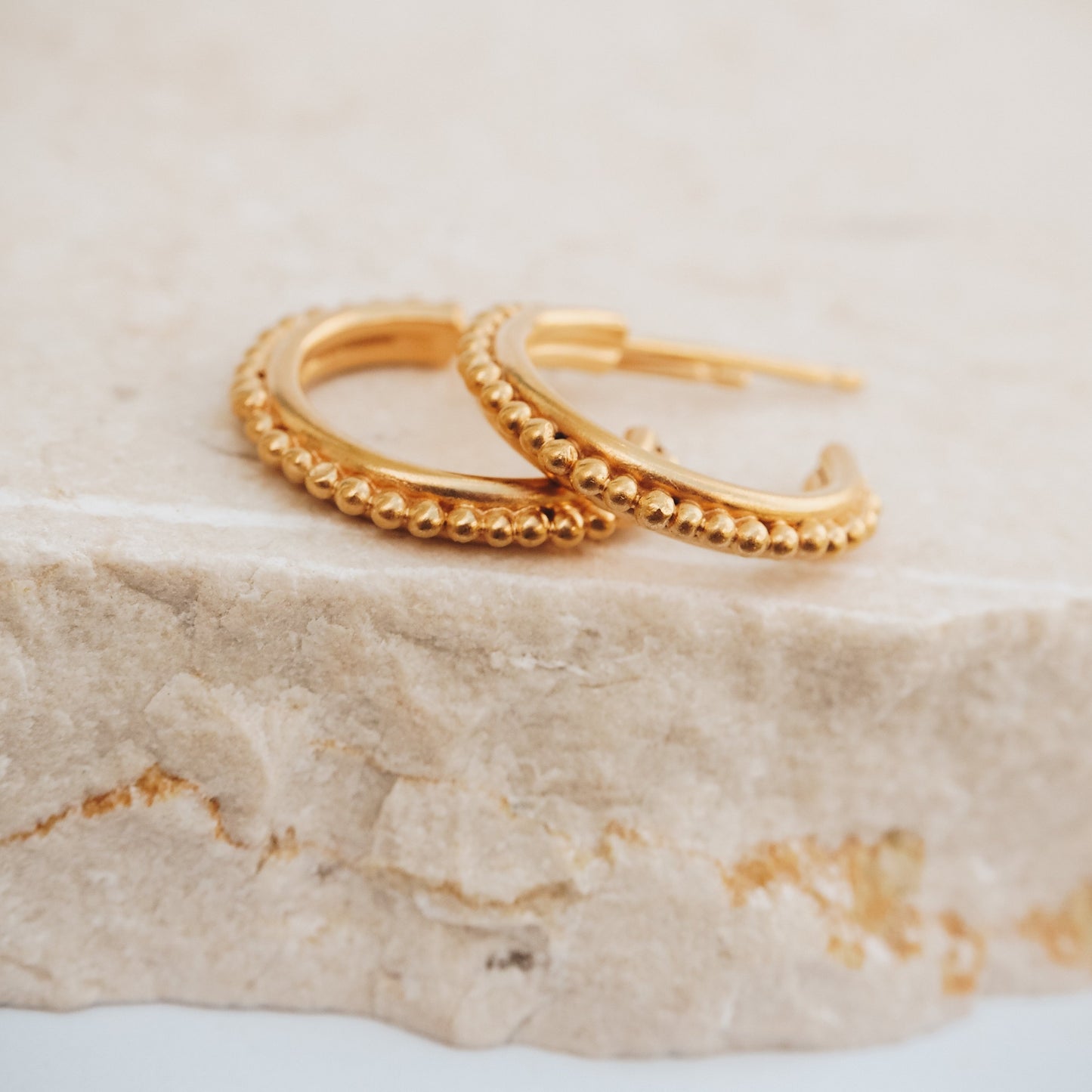 Gold stud hoop earrings with intricate granulation detail, capturing the essence of ancient adornment.