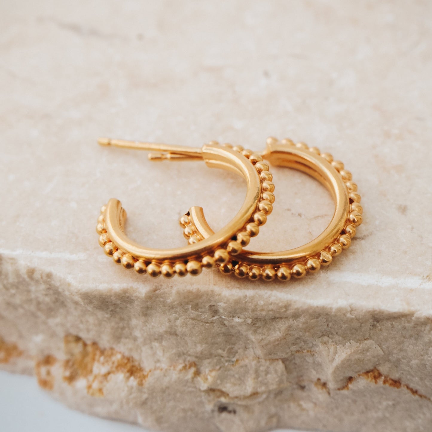 Pair of gold stud hoop earrings with intricate granulation detailing, evoking ancient adornment.