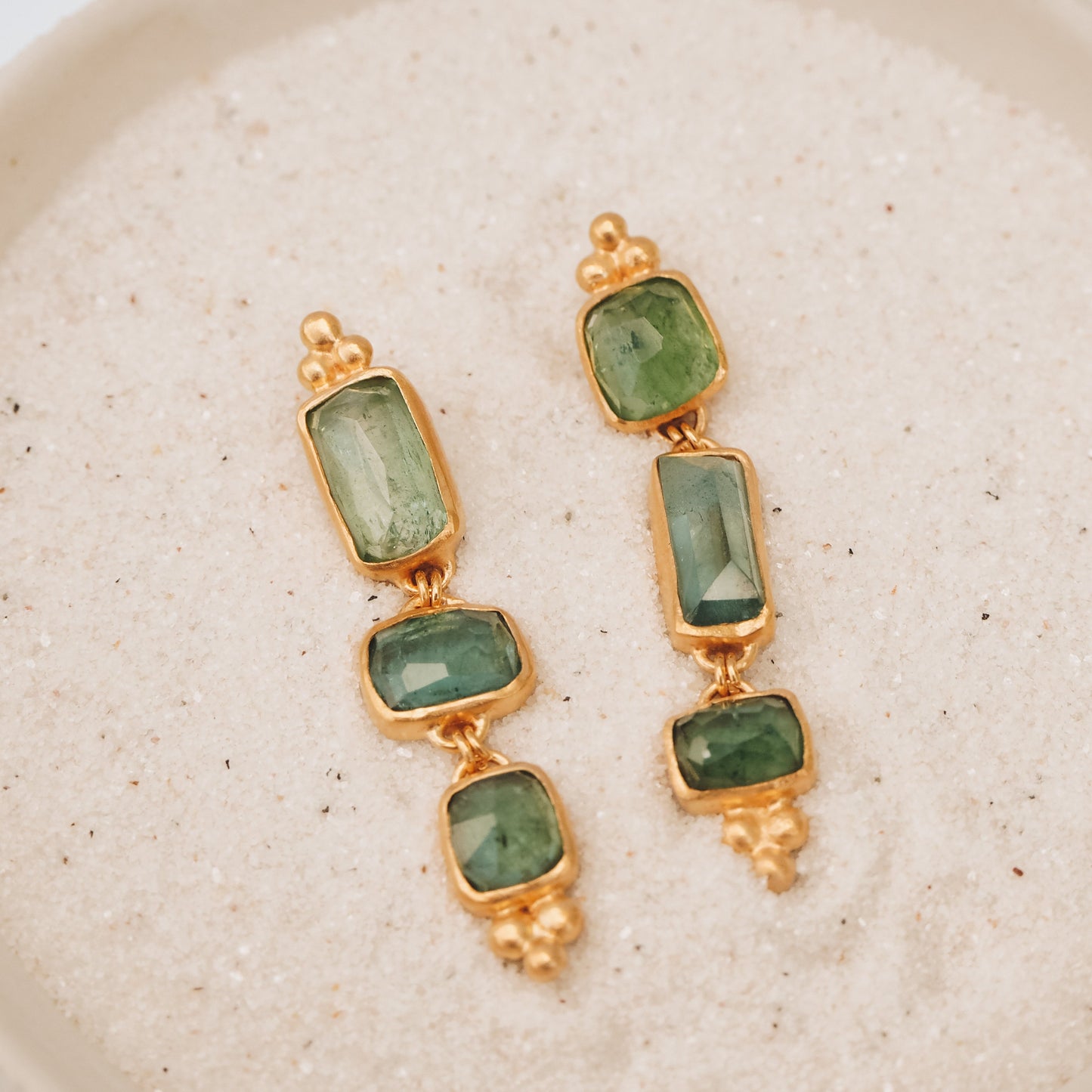 Unique gold earrings featuring one-of-a-kind square rose cut tourmaline gemstone drops in ocean blue and green, accompanied by intricate granulation accents.