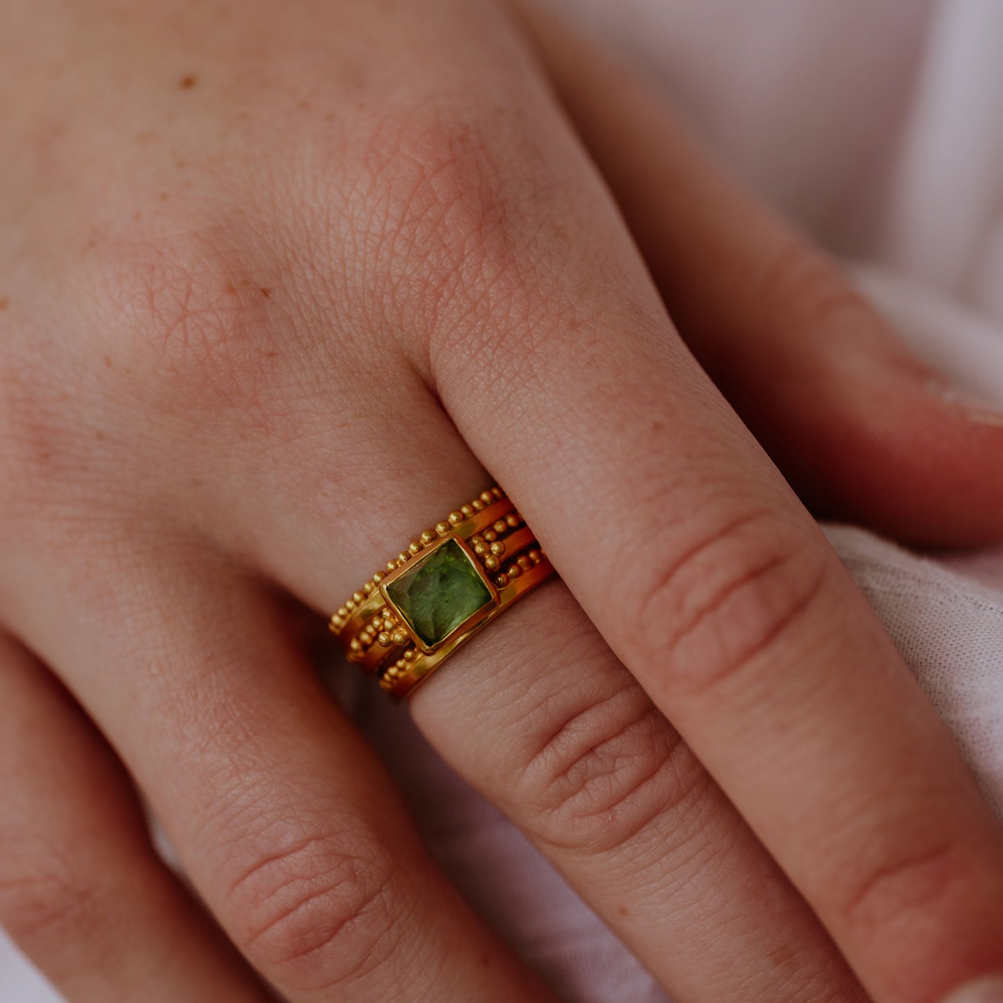 A stack of rich god rings centred around a striking square green tourmaline, each ring featuring intricate granulation detailing.
